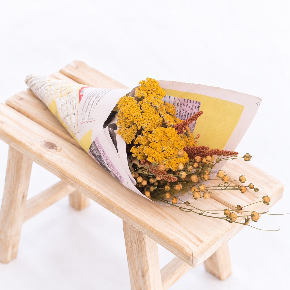 Botte composée d’achillée jaune, de lin et d’amarante terracotta emballée dans du papier recyclé