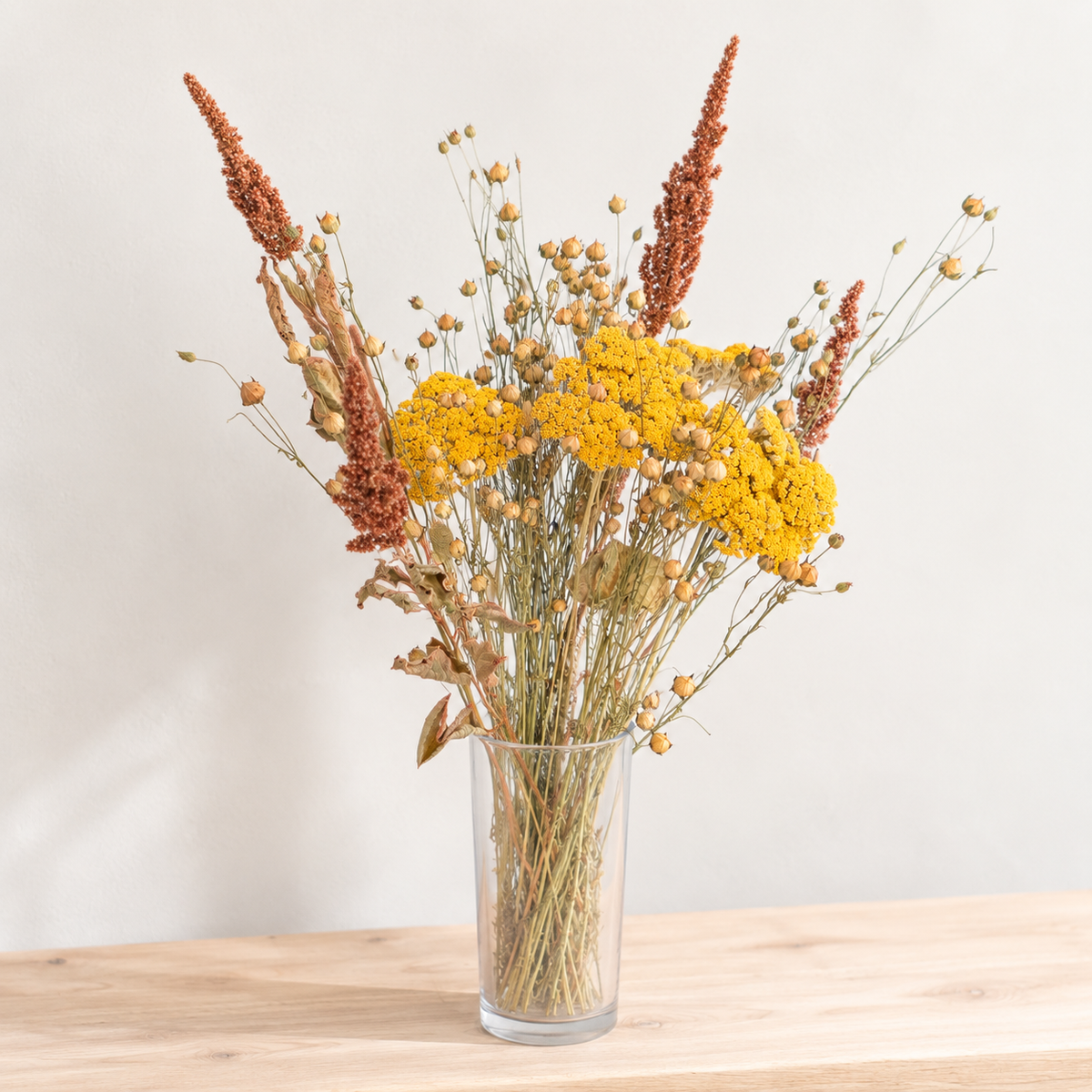 Composition de fleurs séchées avec achillée jaune, lin et amarante terracotta présentée dans un vase transparent