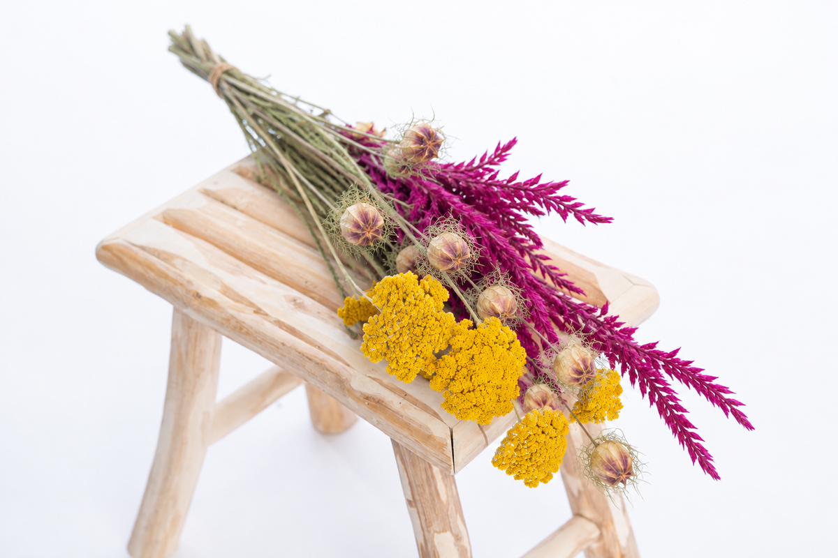 Botte composée de fleurs séchées avec achillée jaune, nigelle et fleur de pays cyclamen sur un banc en bois clair