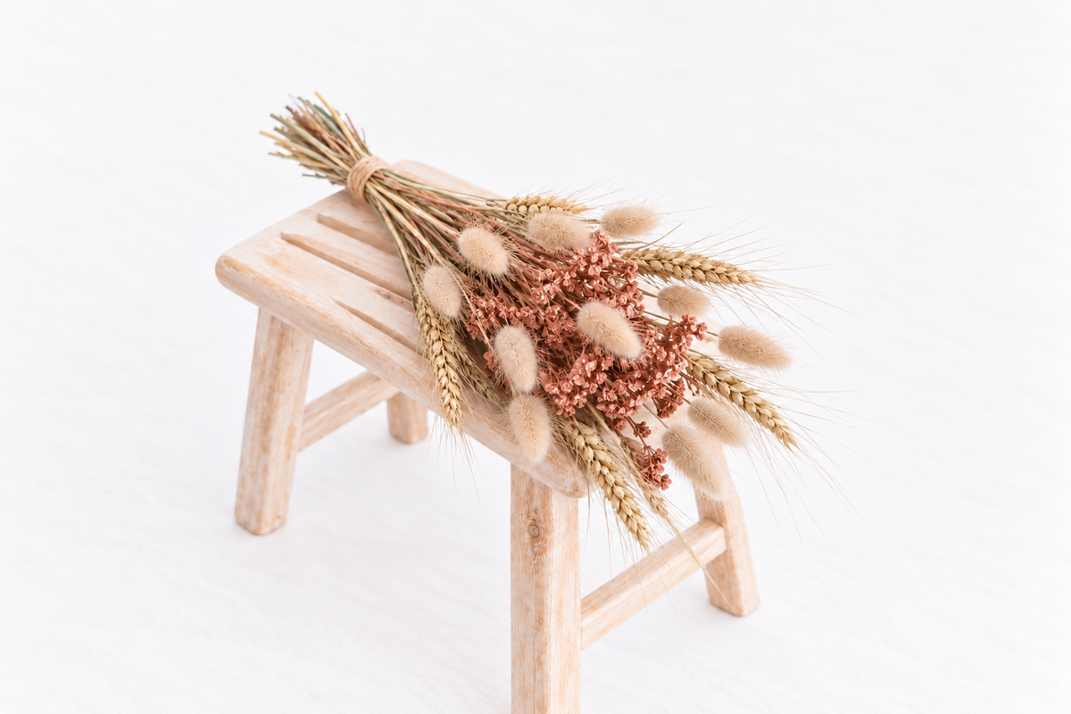 Botte composée d’achillée terracotta, de blé barbu et de lagurus séchés sur un banc en bois clair