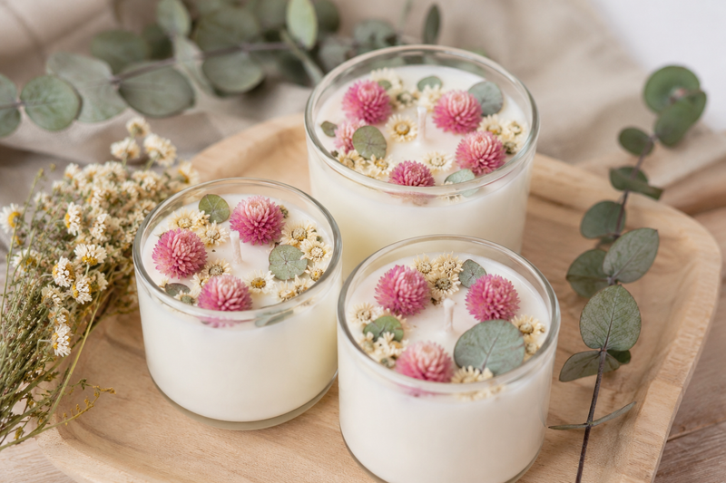 Trois bougies décorées avec des fleurs séchées de gomphrena rose, matricaire et eucalyptus, idée DIY naturelle.