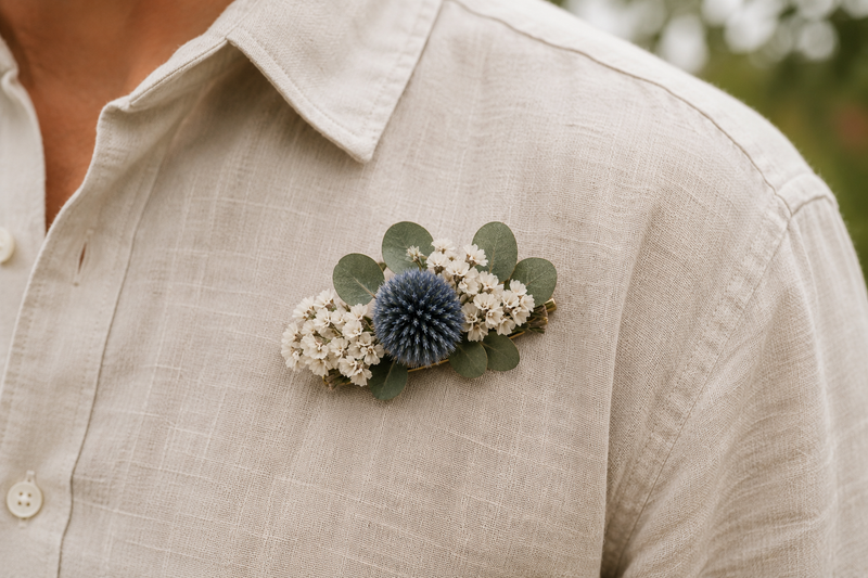 Broche en fleurs séchées portée sur une chemise en lin, composée d'échinops, de statice blanc et d'eucalyptus
