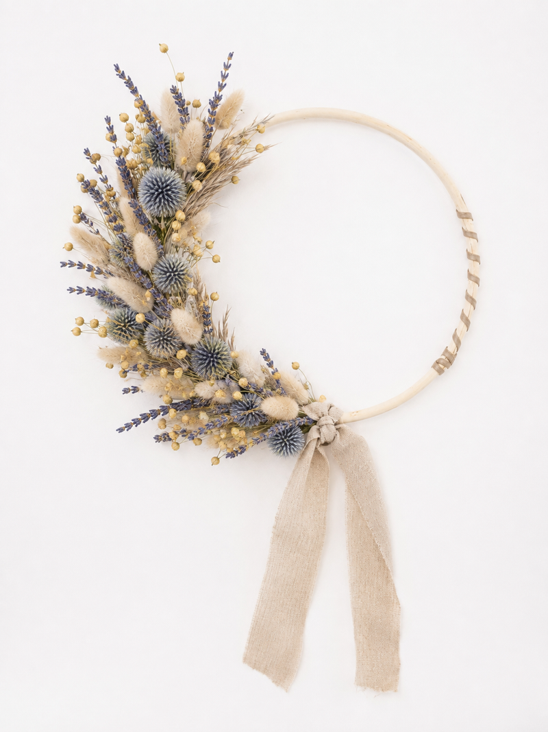 Couronne de fleurs séchées avec échinops bleus, lagurus et lin, accrochée au mur.
Titre : Couronne aux tons naturels et bleus