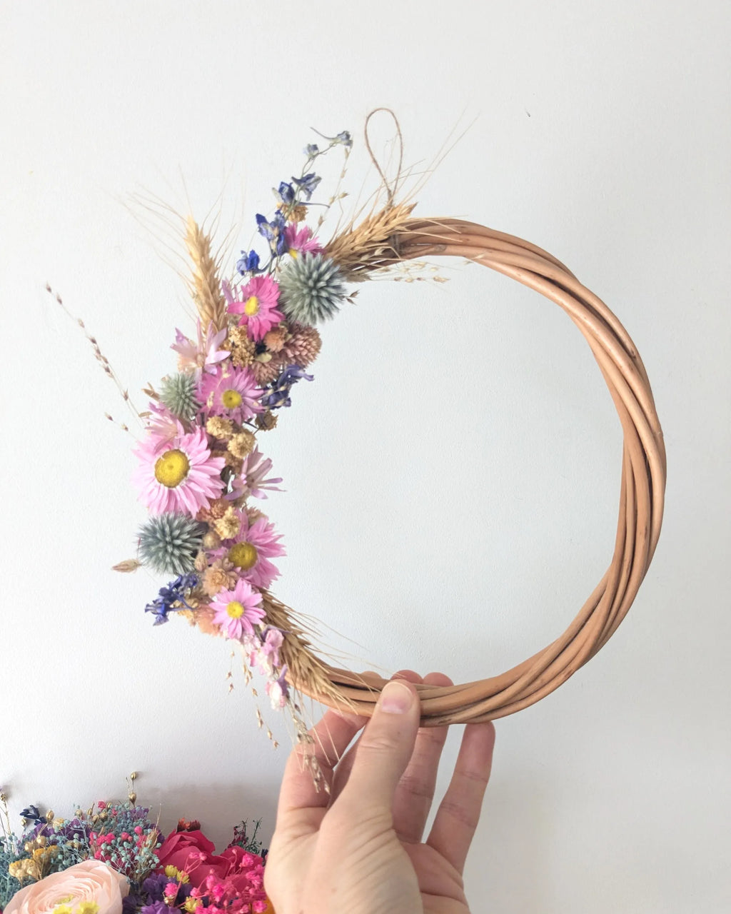 Couronne en fleurs séchées bio du kit Signature Les Pensées de Lily tenue à la main, composée de gomphrena rose, delphinium et fleurs séchées naturelles.