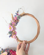 Couronne en fleurs séchées bio du kit Signature Les Pensées de Lily tenue à la main, composée de gomphrena rose, delphinium et fleurs séchées naturelles.